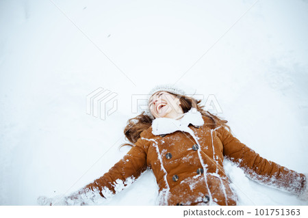 smiling stylish woman in sheepskin coat making snow angels 101751363
