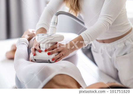 Female beautician holds LPG endermology device with both hands scanning the female body of her client 101751820