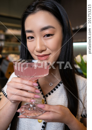 Pleased female lifting a glass of cocktail to her lips Pleased female lifting a glass of cocktail to her lips 101753215