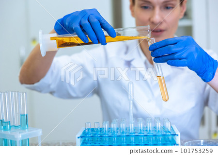 Woman biologist holding test tubes, pouring yellow liquid in flask with concentrated look 101753259