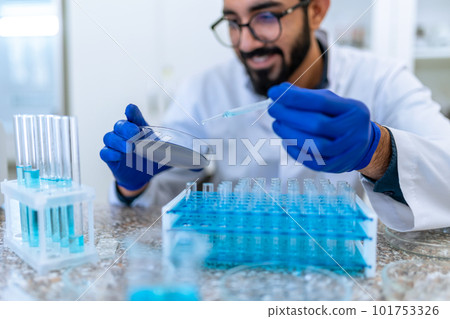 Smiling scientist man testing chemical sample in flask at laboratory with lab glassware. Smiling scientist man testing chemical sample in flask at laboratory with lab glassware. 101753326