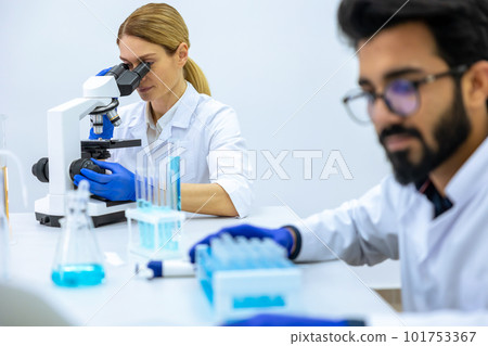 Team of scientists examining sample, using microscope and chemical liquids in flask in modern lab 101753367