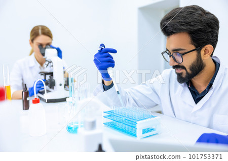 Team of scientists examining sample, using microscope and chemical liquids in flask in modern lab 101753371