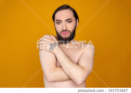 Serious naked transgender person with beard standing with crossed hands on chest hiding body Serious naked transgender person with beard standing with crossed hands on chest hiding body 101753887
