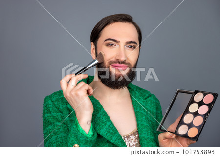 Transsexual person wearing green jacket holding brush and palette of eye shadows, doing makeup Transsexual person wearing green jacket holding brush and palette of eye shadows, doing makeup 101753893