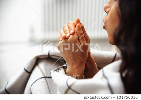 Cold apartment. A young woman tries to keep warm by wrapping in a blanket  101756016