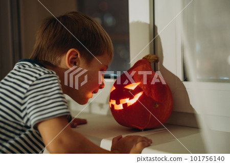 Little boy looking at self made e traditional Jack lantern. Candle lame reflection on his face Little boy looking at self made e traditional Jack lantern. Candle lame reflection on his face 101756140