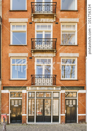 a brick building with many windows and bales on the top floor, in front of it is a fire hydrator 101756334