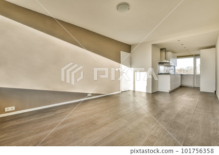 an empty living room with wood flooring and white trim on the walls there is a kitchen in the background 101756358