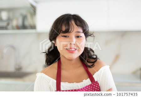 Positive woman in apron standing at kitchen interior near countertop Positive woman in apron standing at kitchen interior near countertop 101757435