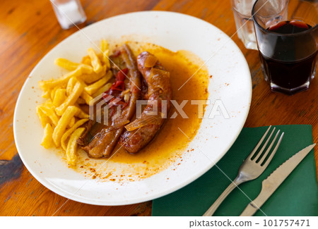 Rustic dish of fried sausage and bacon with French fries on a plate on a wooden table in the canteen 101757471
