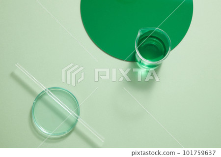 A beaker containing green liquid decorated with a round green plastic board and a glass rod put on top of a petri dish. Empty space for product promotion. copy space 101759637