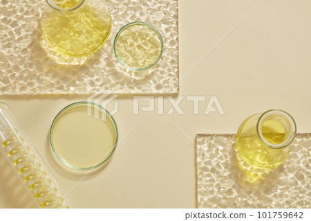 Flat lay of erlenmeyer flasks, petri dish and a test tube with spiral pipe inside containing yellow liquid. Cosmetic laboratory research and development content 101759642