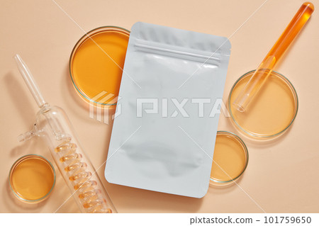 A mask sheet with unlabeled packaging decorated with petri dishes and test tube of orange liquid. Natural organic beauty cosmetics concept. Research content. Branding mockup 101759650