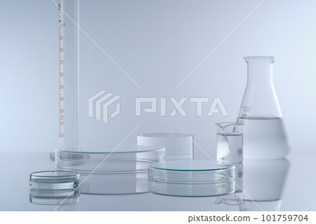 Minimal background with laboratory glassware containing colorless liquid decorated on white background. Two petri dishes upside down form empty platforms to cosmetic product presentation. Front view. 101759704