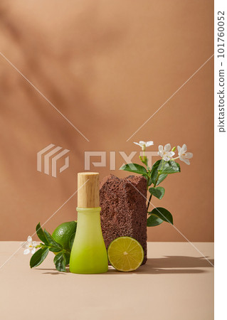 A jar with gradient color displayed with Lime slice, a stone and white flowers on brown background. Lime (Citrus aurantiifolia) can remove the stratum corneum and dead skin cells 101760052