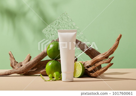 A white tube without label arranged with Lime slice and peels against pastel green background. Lime (Citrus aurantiifolia) is high in vitamin C that can help whitening skin 101760061