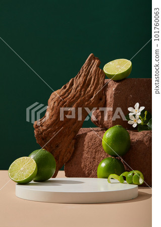 A stack of stones displayed with small white flowers, tree branch, Lime halves and peels. White round podium with empty space for organic product promotion of Lime (Citrus aurantiifolia) extract 101760063