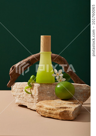 An unlabeled green gradient jar put on a stone block decorated with Lime and white flowers. Lime (Citrus aurantiifolia) helps lighten dark spots as a natural bleaching agent 101760065