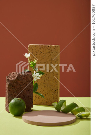 Front view of round empty podium,stones, fresh lime, spiral lime peel and flower branch decorated on color background. Blank space for display cosmetic of lime extract with minimal concept. 101760087
