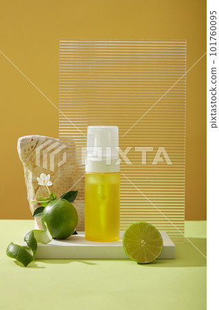 Front view of yellow spray bottle unlabeled on podium, halves of lime, peel, flower, rock and acrylic sheet on yellow background. Mockup scene for product of natural extract - rich in vitamin C. 101760095