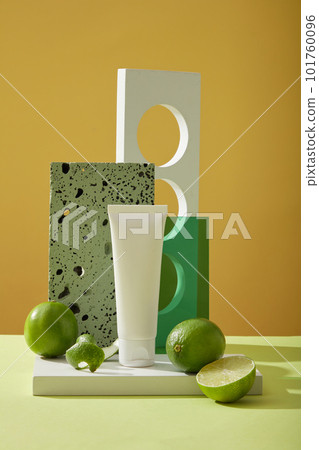 Scene of bottle unlabeled on podium, fresh limes, gray brick and geometric object on yellow background. Mockup for facial cleanser extracted from limes to strengthen, support facial cleansing 101760096
