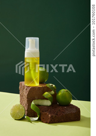 Front view of yellow spray bottle unlabeled placed on brown stone podiums and fresh limes decorated on dark background. Mockup scene for cosmetic product of lime extract. Minimal concept 101760108