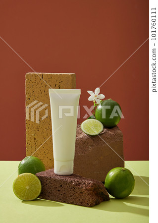 Mockup scene with empty bottle unlabeled for cosmetic product of lime extract. Fresh limes and small white flower placed on dark stones on color background. Front view, space for design Mockup scene with empty bottle unlabeled for cosmetic product of lime extract. Fresh limes and small white flower placed on dark stones on color background. Front view, space for design 101760111