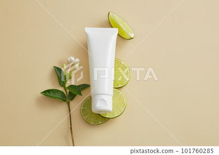 White tube placed on several Lime slices and decorated with a flower branch beside. Lime (Citrus aurantiifolia) helps lighten dark spots as a natural bleaching agent 101760285