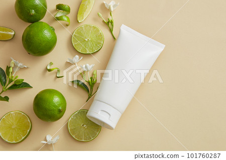 Against a beige background, some Lime (Citrus aurantiifolia) slices, peels and flower branches are arranged with a white tube. Product mockup with empty label. copy space in the right side Against a beige background, some Lime (Citrus aurantiifolia) slices, peels and flower branches are arranged with a white tube. Product mockup with empty label. copy space in the right side 101760287
