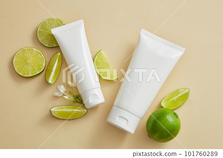 Two empty label tubes arranged with Lime slices and mini white flowers. Organic beauty product mockup with Lime (Citrus aurantiifolia) extract 101760289