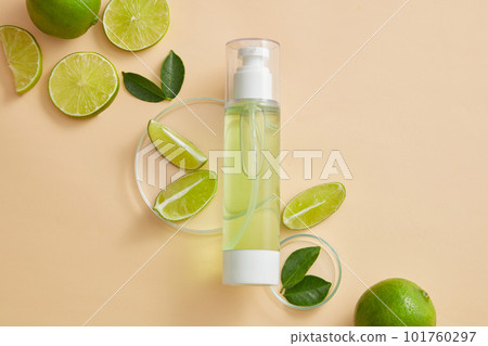 Empty label pump bottle dispenser displayed on beige background with petri dishes of Lime (Citrus aurantiifolia) slices and green leaves. Toner or serum cosmetic product promotion 101760297