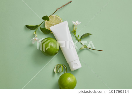 Top view of a white tube with empty label decorated with some Limes and white flower branches. Lime (Citrus aurantiifolia) is used in production of cosmetic as ingredient 101760314