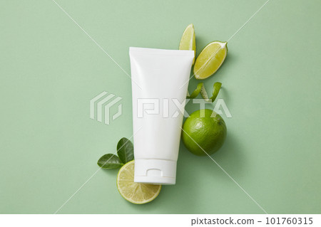 Flat lay of an empty label tube arranged with several Lime slices and green leaves on minimal light background. Lime (Citrus aurantiifolia) has properties that may promote healthy skin 101760315