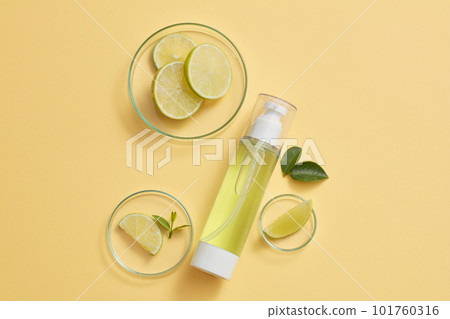Several Lime slices placed on some glass petri dishes, a transparent pump bottle filled with yellow liquid. Concept of soothing natural beauty product extracted from Lime (Citrus aurantiifolia) 101760316