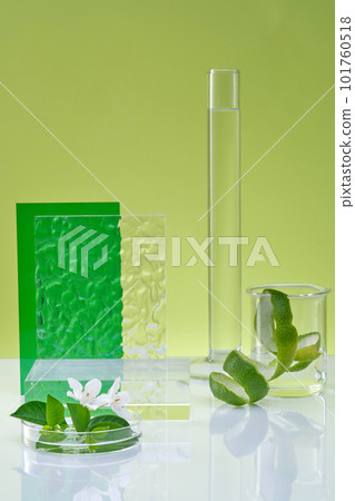 Front view of lab glassware, spiral lime peel and white flower, green leaves on green background. Empty podium for display cosmetic of lime extract. Research and production of natural cosmetics 101760518