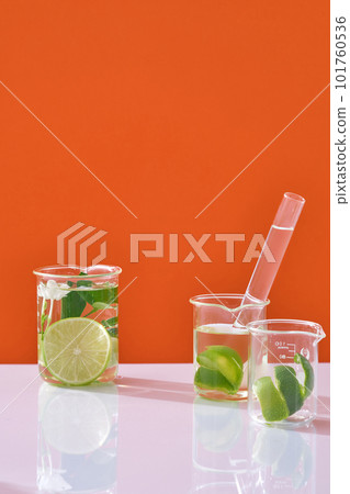 Lime slices, peel and green leaves in beakers and colorless liquid decorated on orange neon background. Scene for advertising cosmetic of natural extract. Blank space for display 101760536