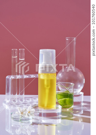 Front view of yellow bottle unlabeled on transparent podium and lab glassware containing liquid decorated on pink background. Mockup for cosmetic product of lime extract rich in vitamin C. Front view of yellow bottle unlabeled on transparent podium and lab glassware containing liquid decorated on pink background. Mockup for cosmetic product of lime extract rich in vitamin C. 101760540