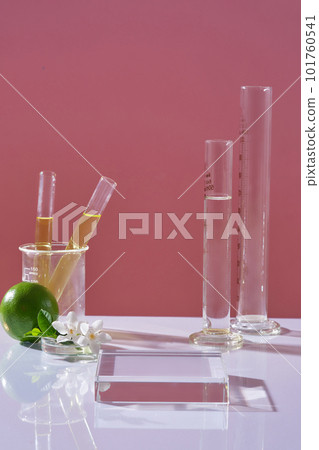 Laboratory concept - test tubes containing yellow liquid, fresh lime and white flowers decorated on pink background. Empty transparent platform for display cosmetics. Laboratory concept - test tubes containing yellow liquid, fresh lime and white flowers decorated on pink background. Empty transparent platform for display cosmetics. 101760541