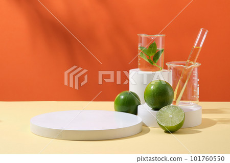 Pedestal for cosmetic product display presentation with round empty podium, limes and lab glassware containing yellow liquid on orange background. Advertising photo, copy space 101760550
