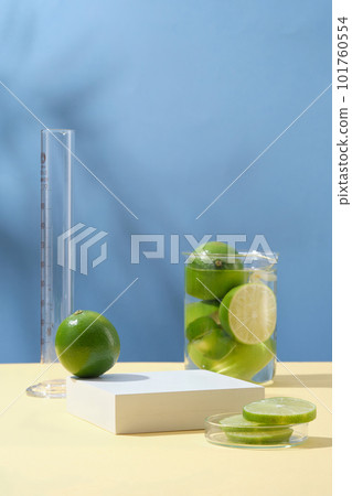 Minimal background with blank space for display cosmetic of lime extract. White empty podium, fresh limes in beaker and petri dish on blue background with natural shadow leaves. Copy space 101760554