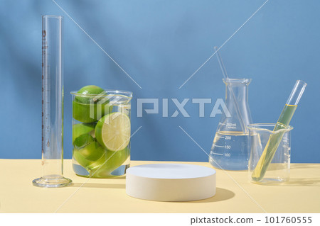 Front view of round empty podium, fresh limes and laboratory glassware containing transparent liquid on blue background. Blank space for display cosmetic of lime extract with minimal concept. Front view of round empty podium, fresh limes and laboratory glassware containing transparent liquid on blue background. Blank space for display cosmetic of lime extract with minimal concept. 101760555