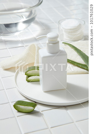 A pump bottle dispenser decorated with Aloe vera slices on a round dish, a glass bowl of water and cotton pads displayed. It helps in gentle cleansing, and its antimicrobial properties treat pimples 101761029