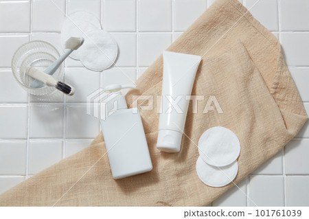 A towel with empty label tube and pump bottle dispenser placed on with cotton pads. A glass with toothbrushes inside. Aloe vera (Aloe barbadensis miller) benefiting skin, hair and teeth also 101761039