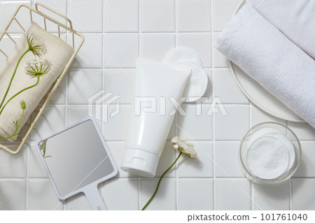 Over white tile background, an unlabeled tube is decorated with cotton pads, flower branches, mirror, towels. Product mockup of Aloe vera extract. It helps to moisturize the skin Over white tile background, an unlabeled tube is decorated with cotton pads, flower branches, mirror, towels. Product mockup of Aloe vera extract. It helps to moisturize the skin 101761040