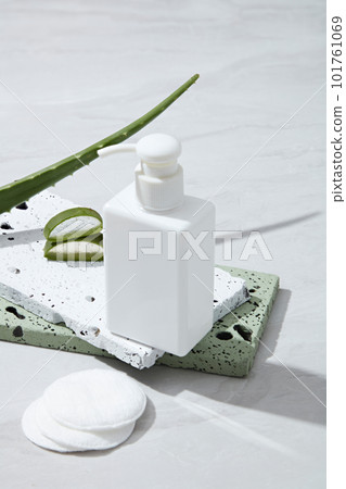 Blank plastic cosmetics container for cream or shampoo on stones podiums, makeup remover cotton and fresh aloe vera leaves decorated on white background. Cosmetic mockup extracted from aloe vera. 101761069