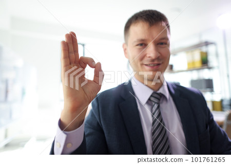 Smiling businessman shows Okay sign sitting in office Smiling businessman shows Okay sign sitting in office 101761265