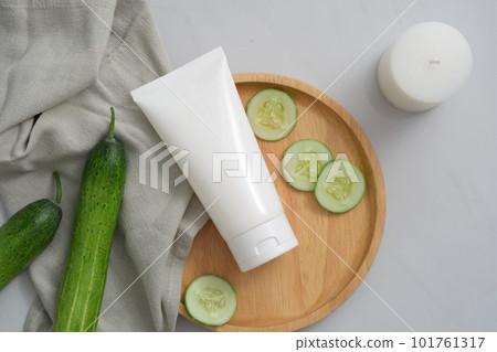 Mockup scene for cosmetics of cucumber extract with copy space - white plastic tube, cucumber slices and gray towel on wooden dishes and scented candles. Background for organic cosmetic concept Mockup scene for cosmetics of cucumber extract with copy space - white plastic tube, cucumber slices and gray towel on wooden dishes and scented candles. Background for organic cosmetic concept 101761317
