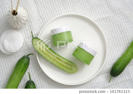 Top view of cream jars and cucumber slices on round dishes, cotton pads and reed diffuser on white fabric background. Mockup for cosmetic of cucumber extract, moisturize, exfoliate and whiten skin Top view of cream jars and cucumber slices on round dishes, cotton pads and reed diffuser on white fabric background. Mockup for cosmetic of cucumber extract, moisturize, exfoliate and whiten skin 101761323