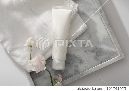 An empty label white tube arranged with a towel and white flower branch on a marble tray. Container packaging of skin care branding An empty label white tube arranged with a towel and white flower branch on a marble tray. Container packaging of skin care branding 101761955